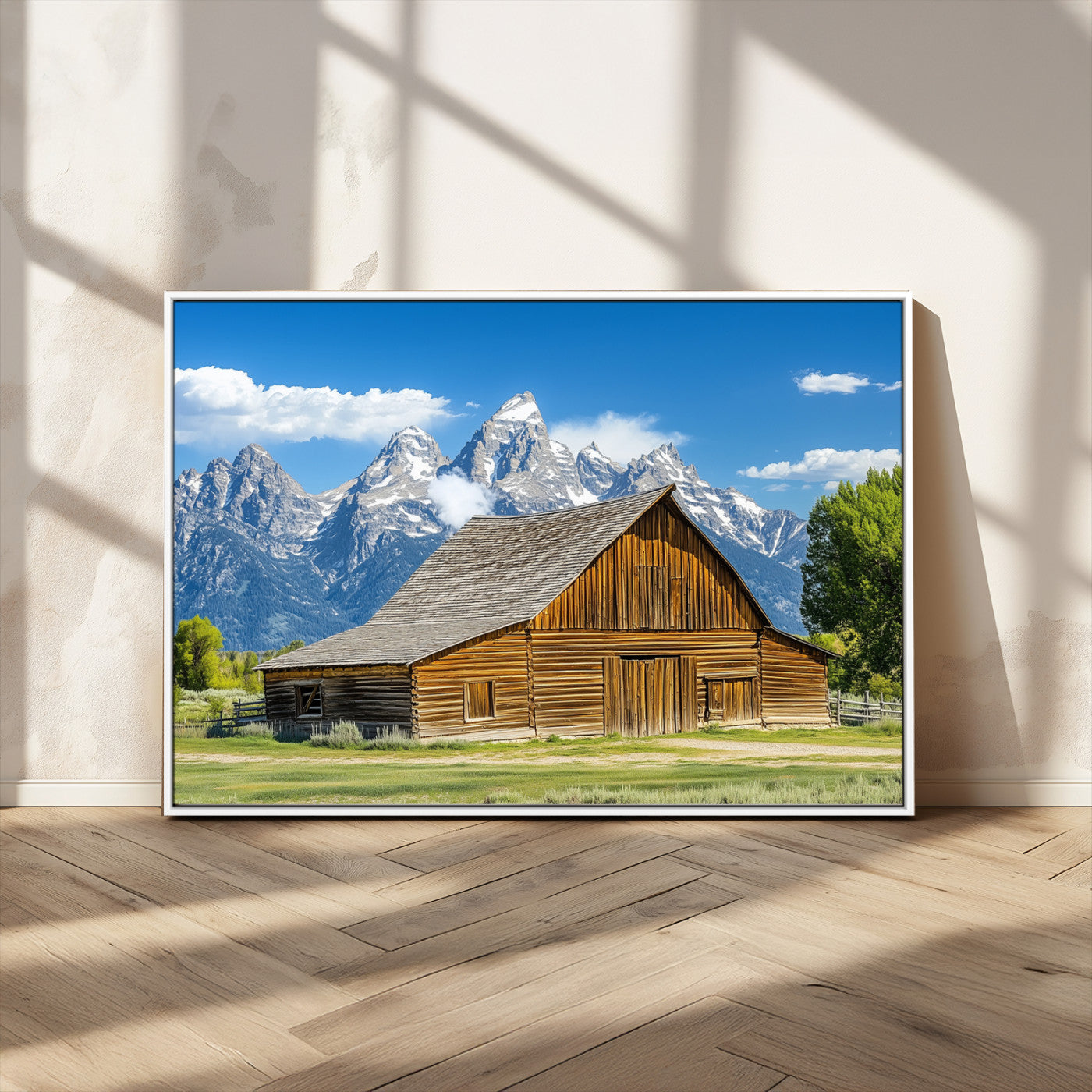 A rustic wooden barn sits in front of towering mountain peaks under a clear blue sky, perfect for farmhouse or cabin style interiors.
