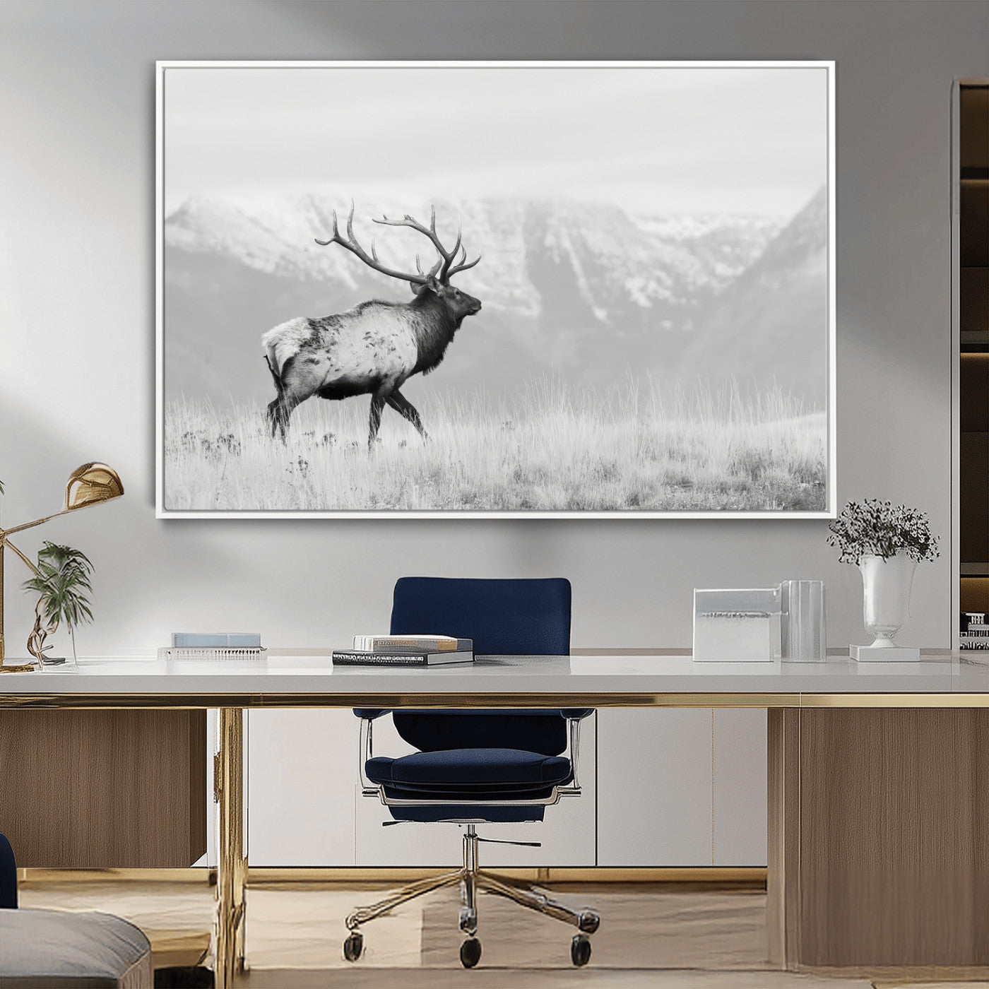 Black and white photograph of a majestic elk standing in a grassy field with snow-capped mountains in the background, creating a bold and rustic wilderness scene.