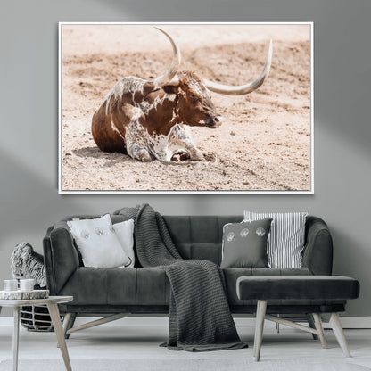 Texas Longhorn bull resting on dusty ground with warm tones, ideal for rustic western or farmhouse-themed wall decor.