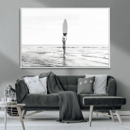 Black and white image of a female surfer holding a surfboard above her head while walking toward the ocean, creating a minimalist and bold coastal aesthetic.