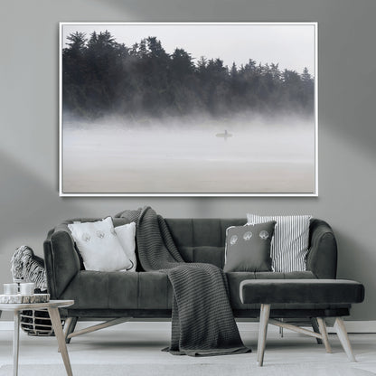 A lone surfer carrying a board through a misty shoreline, surrounded by dense trees and fog, creating a peaceful and mysterious coastal scene.