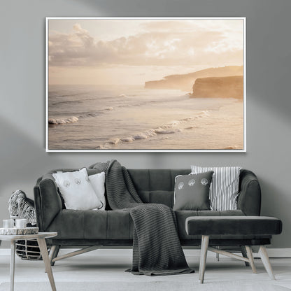 Golden hour seascape with misty cliffs and gentle waves rolling towards the shore, capturing a tranquil and warm coastal atmosphere.