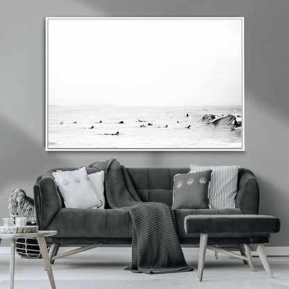 A group of surfers floating in the ocean, waiting for waves under a vast, moody sky, captured in black and white.