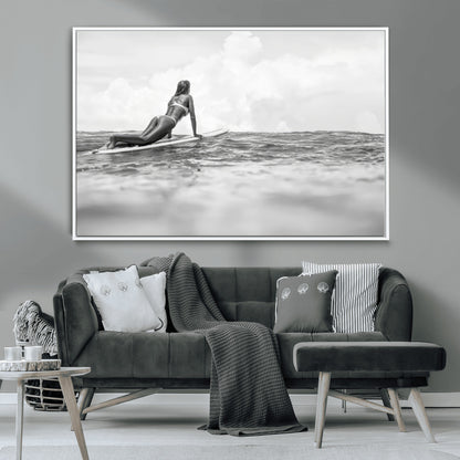 A black and white ocean scene featuring a surfer girl waiting on her board, gazing at the horizon, capturing a tranquil and adventurous coastal moment.