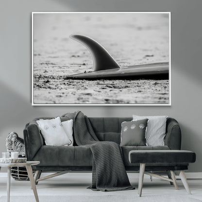 A black and white close-up of a surfboard fin resting on the sandy shore, highlighting minimalist beach aesthetics and classic surf culture.