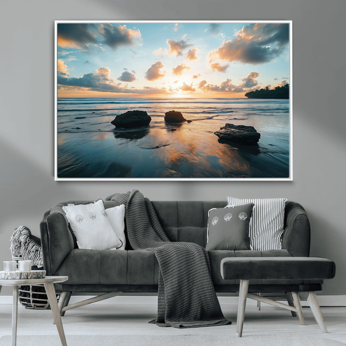 A serene beach at sunset with vibrant clouds, calm water, and rocks in the foreground reflecting the warm colors of the setting sun.