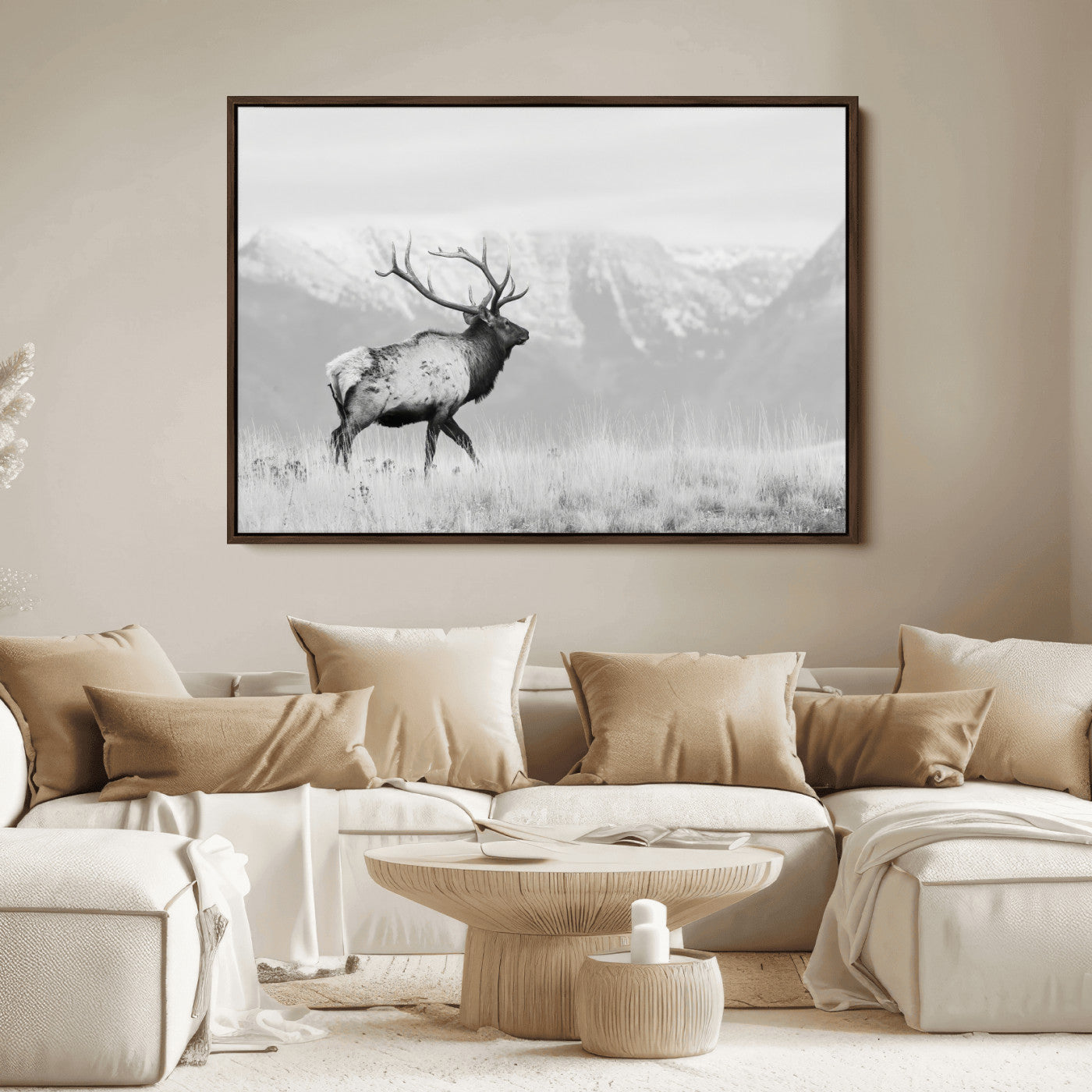 Black and white photograph of a majestic elk standing in a grassy field with snow-capped mountains in the background, creating a bold and rustic wilderness scene.