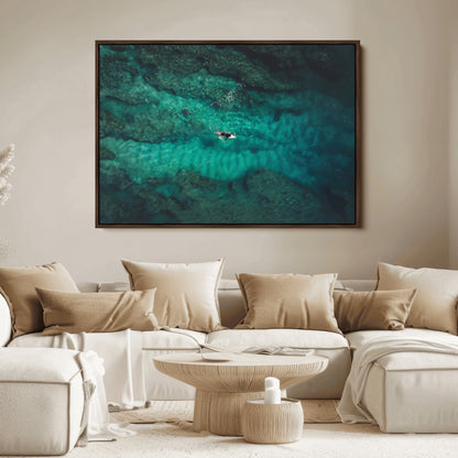 An aerial view of a solo surfer paddling through crystal-clear turquoise waters over a sunlit reef, capturing the beauty and serenity of open water surfing.
