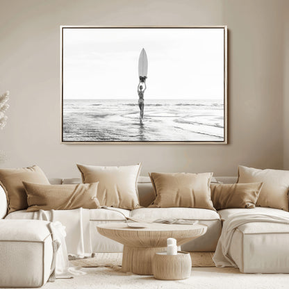 Black and white image of a female surfer holding a surfboard above her head while walking toward the ocean, creating a minimalist and bold coastal aesthetic.