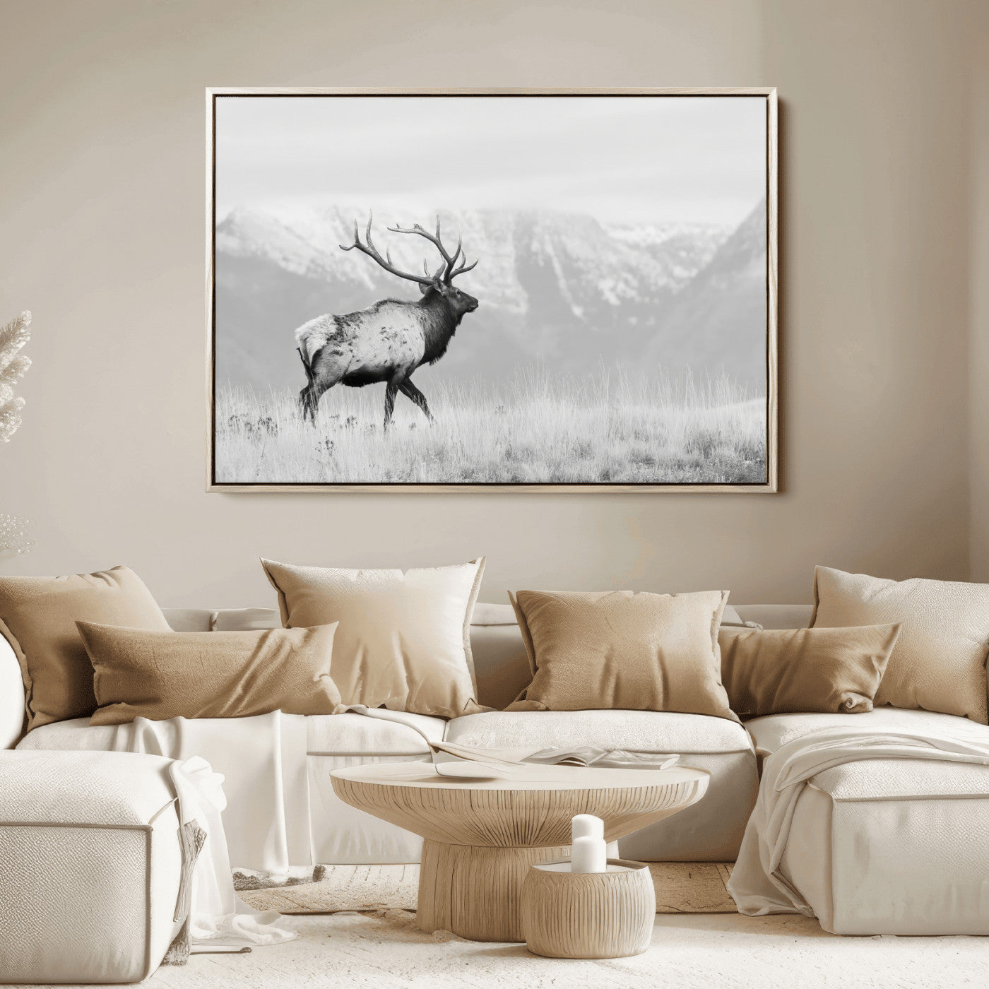 Black and white photograph of a majestic elk standing in a grassy field with snow-capped mountains in the background, creating a bold and rustic wilderness scene.