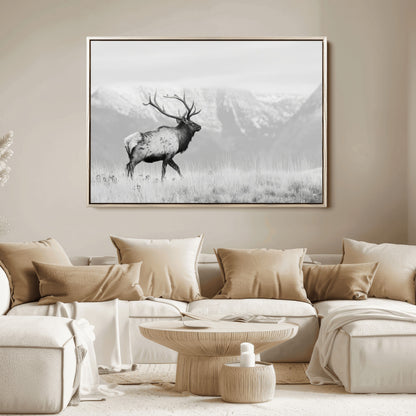Black and white photograph of a majestic elk standing in a grassy field with snow-capped mountains in the background, creating a bold and rustic wilderness scene.