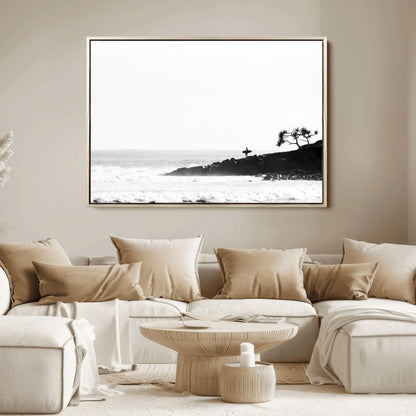 Black and white photo of a surfer standing on rocky cliffs, gazing at the waves, embodying the spirit of adventure and solitude.