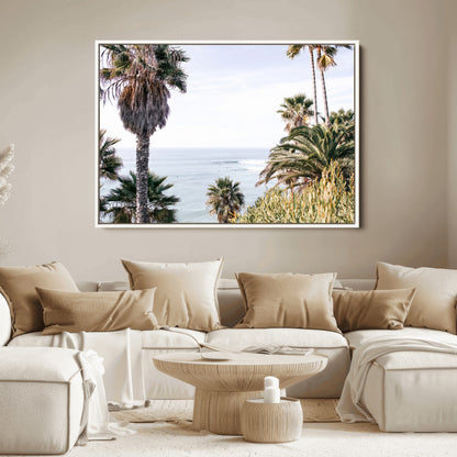 Scenic coastal view with tall palm trees overlooking a calm ocean, soft blue waves, and surfers in the distance, creating a peaceful tropical vibe.