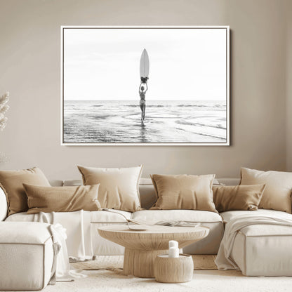 Black and white image of a female surfer holding a surfboard above her head while walking toward the ocean, creating a minimalist and bold coastal aesthetic.