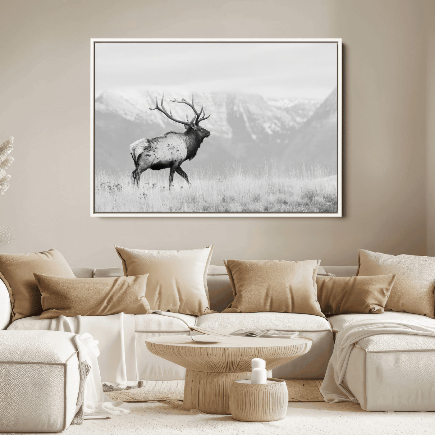 Black and white photograph of a majestic elk standing in a grassy field with snow-capped mountains in the background, creating a bold and rustic wilderness scene.