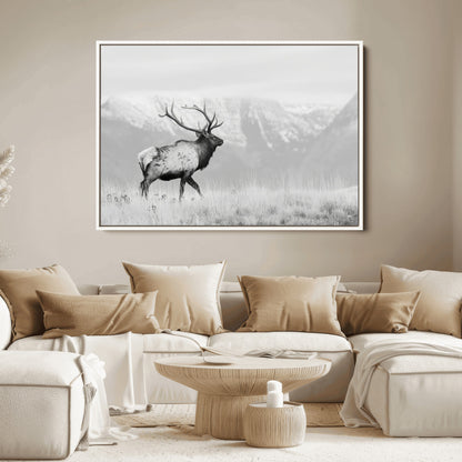 Black and white photograph of a majestic elk standing in a grassy field with snow-capped mountains in the background, creating a bold and rustic wilderness scene.