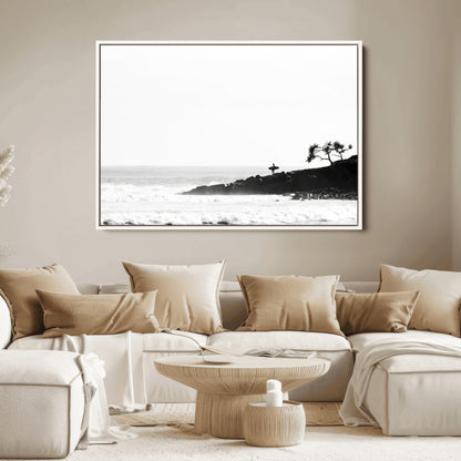 Black and white photo of a surfer standing on rocky cliffs, gazing at the waves, embodying the spirit of adventure and solitude.