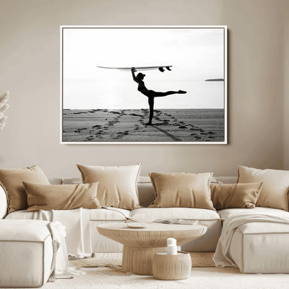 A woman balances a surfboard on her head while striking a yoga pose on the beach, silhouetted against a calm ocean horizon.