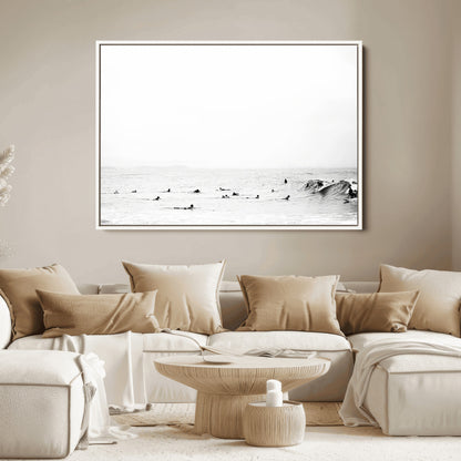 A group of surfers floating in the ocean, waiting for waves under a vast, moody sky, captured in black and white.