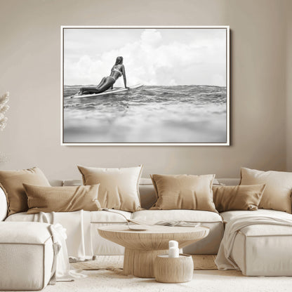 A black and white ocean scene featuring a surfer girl waiting on her board, gazing at the horizon, capturing a tranquil and adventurous coastal moment.