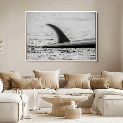 A black and white close-up of a surfboard fin resting on the sandy shore, highlighting minimalist beach aesthetics and classic surf culture.