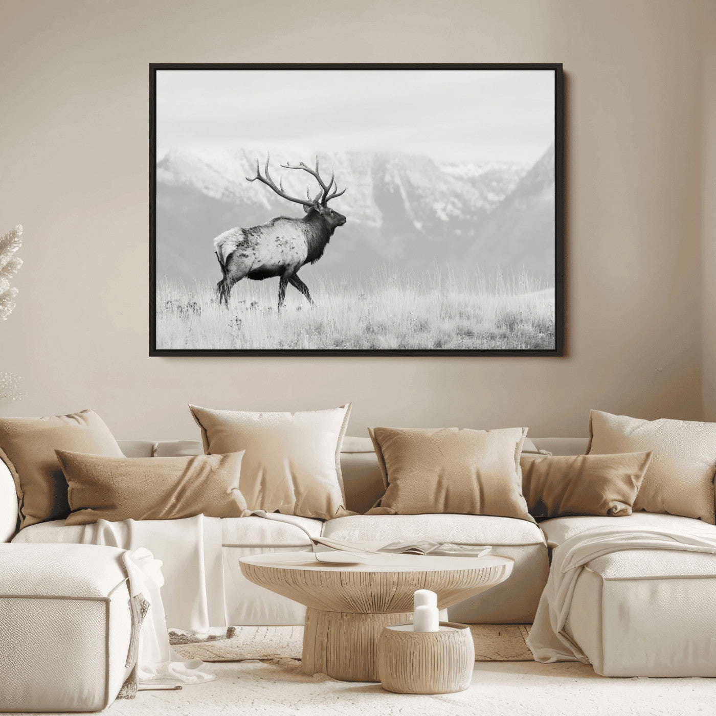 Black and white photograph of a majestic elk standing in a grassy field with snow-capped mountains in the background, creating a bold and rustic wilderness scene.