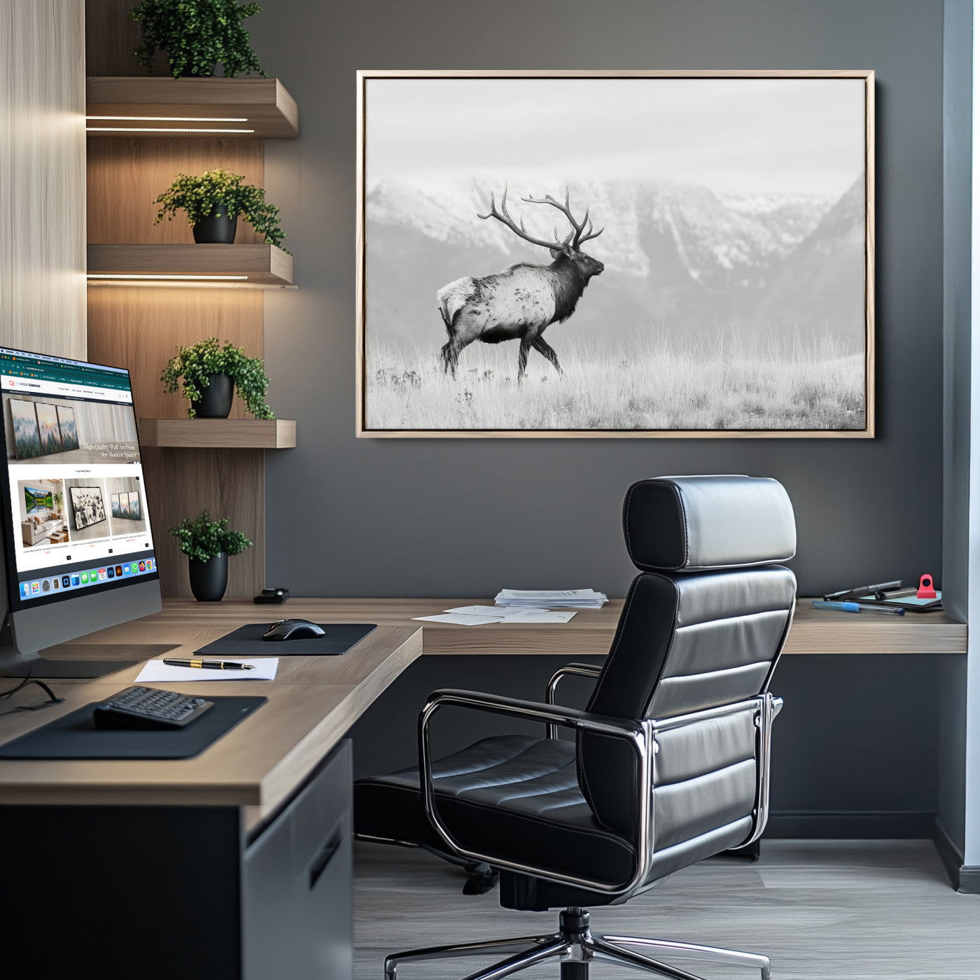 Black and white photograph of a majestic elk standing in a grassy field with snow-capped mountains in the background, creating a bold and rustic wilderness scene.
