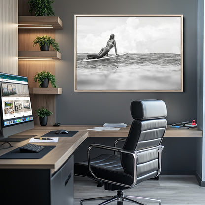 A black and white ocean scene featuring a surfer girl waiting on her board, gazing at the horizon, capturing a tranquil and adventurous coastal moment.