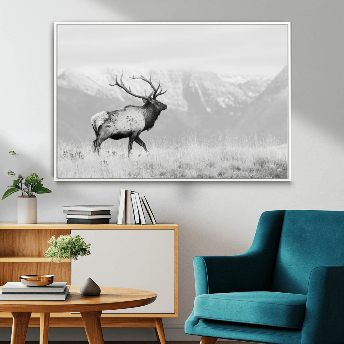 Black and white photograph of a majestic elk standing in a grassy field with snow-capped mountains in the background, creating a bold and rustic wilderness scene.