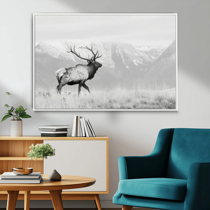 Black and white photograph of a majestic elk standing in a grassy field with snow-capped mountains in the background, creating a bold and rustic wilderness scene.