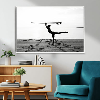 A woman balances a surfboard on her head while striking a yoga pose on the beach, silhouetted against a calm ocean horizon.