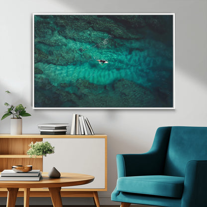 An aerial view of a solo surfer paddling through crystal-clear turquoise waters over a sunlit reef, capturing the beauty and serenity of open water surfing.