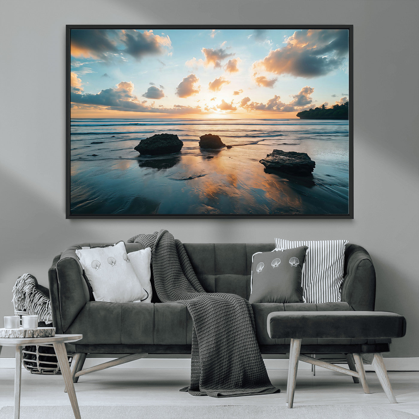 A serene beach at sunset with vibrant clouds, calm water, and rocks in the foreground reflecting the warm colors of the setting sun.