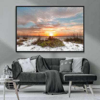 A tranquil beach scene featuring golden sunset hues over the water, with grasses in the foreground and a peaceful, serene atmosphere.