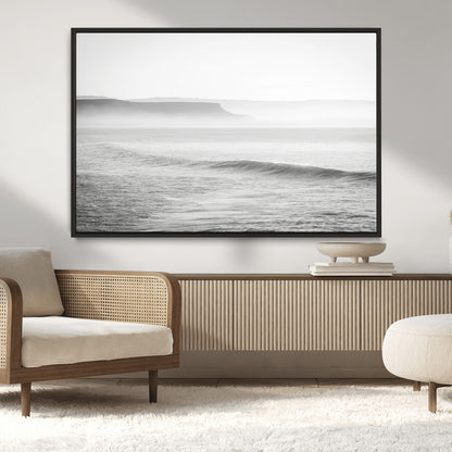 A black and white minimalist seascape featuring soft rolling waves and misty distant cliffs, creating a serene and timeless coastal atmosphere.