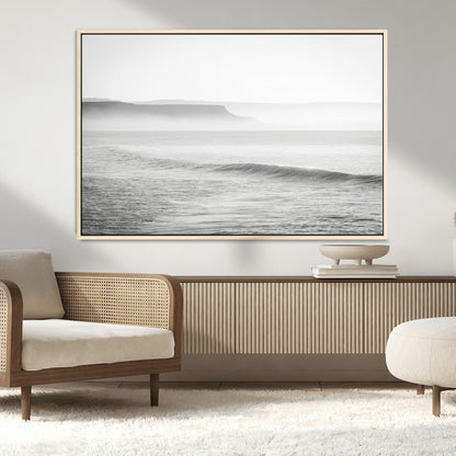 A black and white minimalist seascape featuring soft rolling waves and misty distant cliffs, creating a serene and timeless coastal atmosphere.