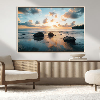 A serene beach at sunset with vibrant clouds, calm water, and rocks in the foreground reflecting the warm colors of the setting sun.