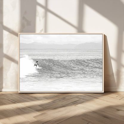 Monochrome photo of a surfer riding a wave with distant mountains, ideal for coastal motion or black and white surf-themed wall decor.
