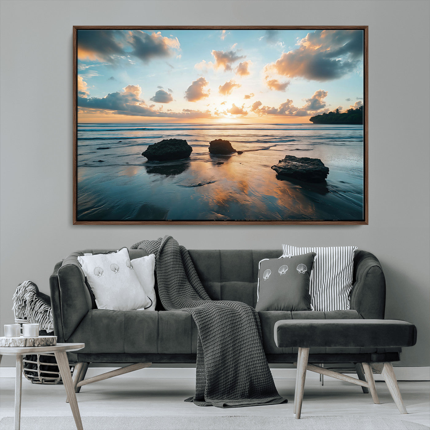 A serene beach at sunset with vibrant clouds, calm water, and rocks in the foreground reflecting the warm colors of the setting sun.