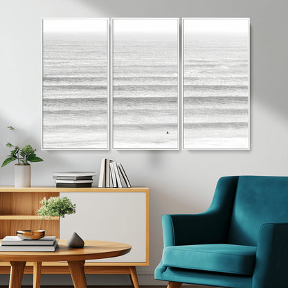 Monochrome photo of a lone surfer in calm layered waves, perfect for minimalist coastal or moody ocean-inspired wall decoration.
