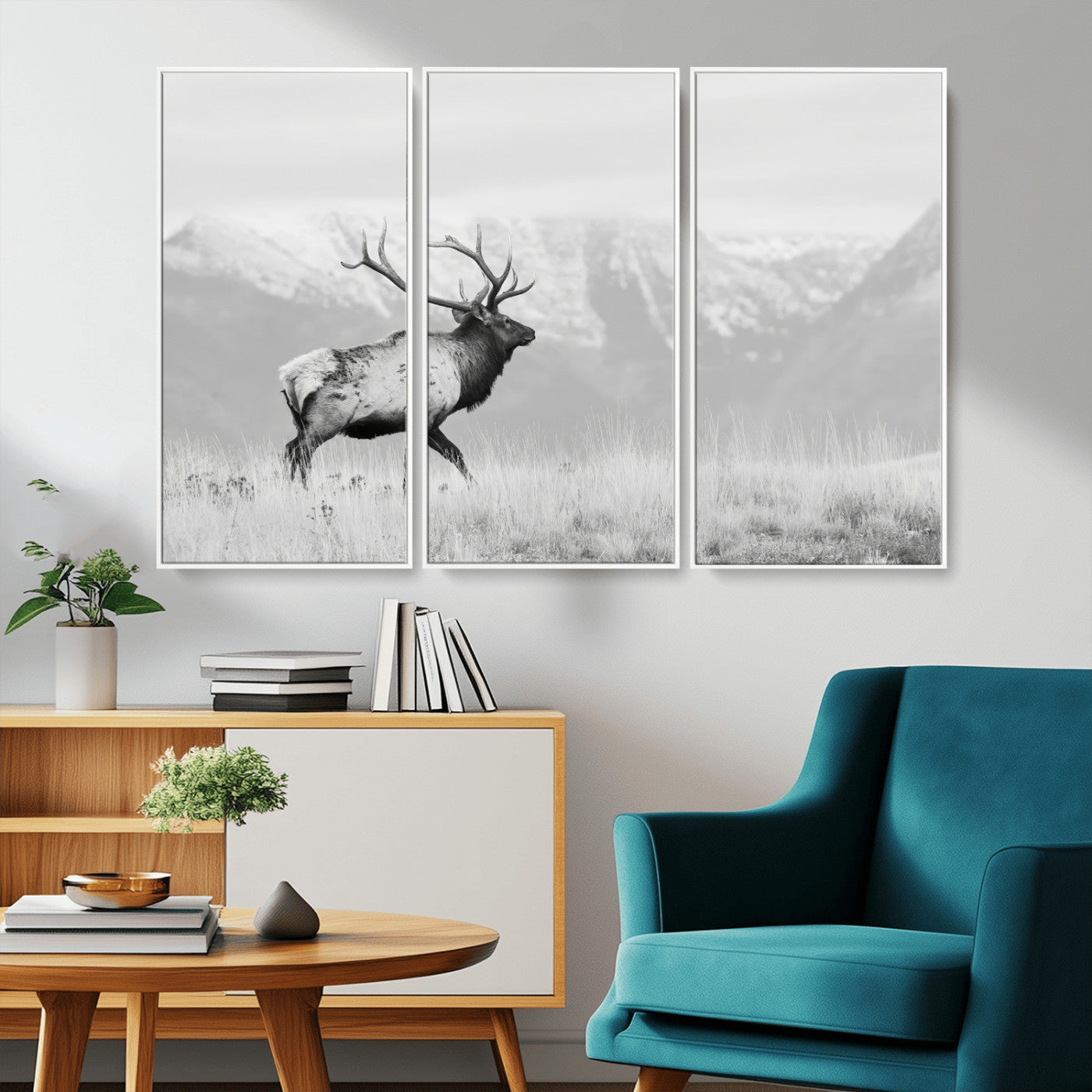 Black and white photograph of a majestic elk standing in a grassy field with snow-capped mountains in the background, creating a bold and rustic wilderness scene.