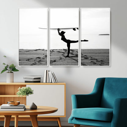 A woman balances a surfboard on her head while striking a yoga pose on the beach, silhouetted against a calm ocean horizon.
