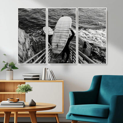 Black and white photo of surfers carrying boards down a rugged cliffside stairway, capturing a bold and adventurous coastal scene.