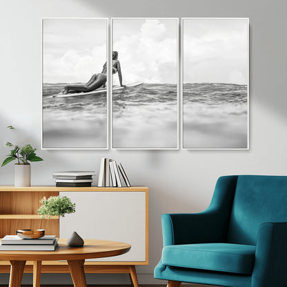 A black and white ocean scene featuring a surfer girl waiting on her board, gazing at the horizon, capturing a tranquil and adventurous coastal moment.