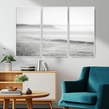 A black and white minimalist seascape featuring soft rolling waves and misty distant cliffs, creating a serene and timeless coastal atmosphere.