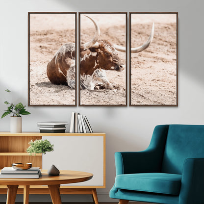 Texas Longhorn bull resting on dusty ground with warm tones, ideal for rustic western or farmhouse-themed wall decor.