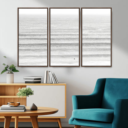 Monochrome photo of a lone surfer in calm layered waves, perfect for minimalist coastal or moody ocean-inspired wall decoration.