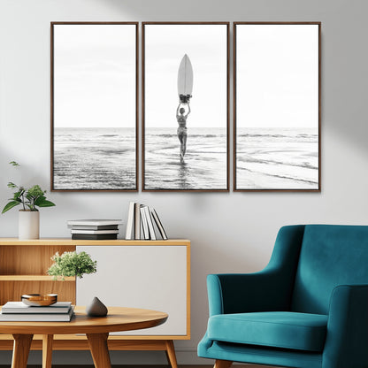 Black and white image of a female surfer holding a surfboard above her head while walking toward the ocean, creating a minimalist and bold coastal aesthetic.