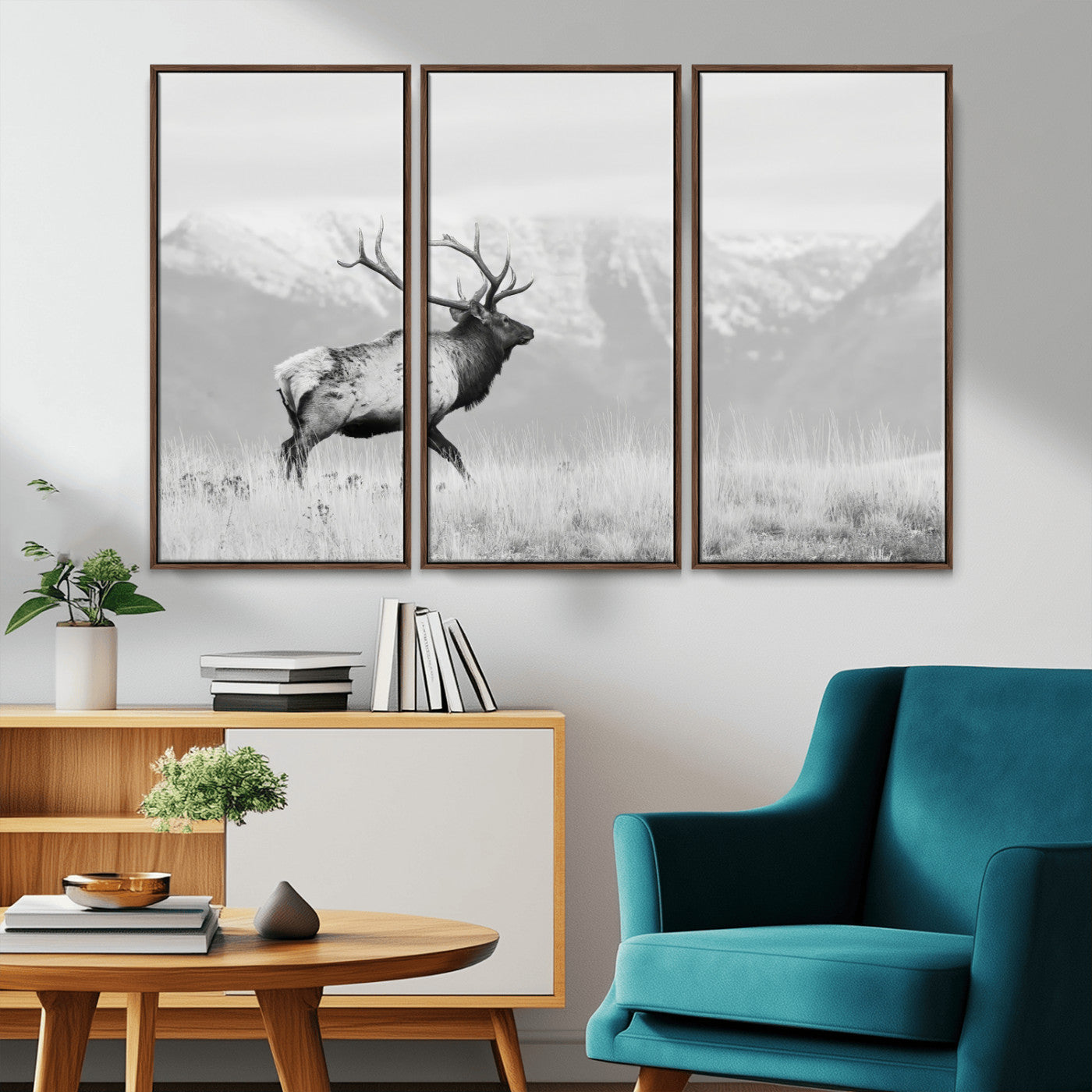 Black and white photograph of a majestic elk standing in a grassy field with snow-capped mountains in the background, creating a bold and rustic wilderness scene.
