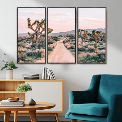 A dusty road winding through Joshua Tree National Park, framed by iconic twisted trees and warm desert tones under a soft pastel sky.